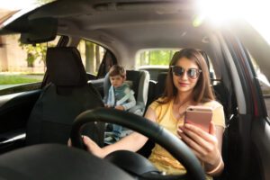 Mother-using-phone-while-driving-car-with-her-son-on-backseat.-Child-in-danger